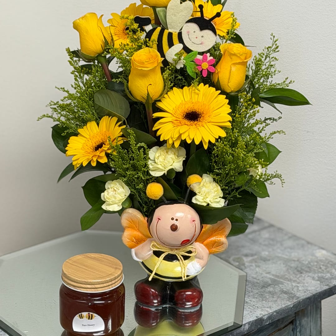 Yellow roses and daisies arranged in a bee-themed vase with a small honey jar beside it.