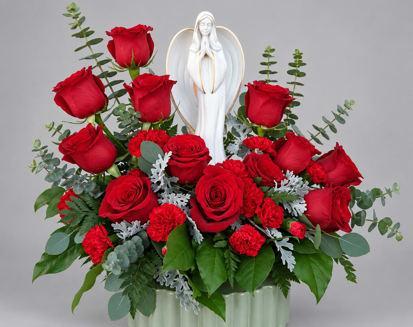 Red roses and carnations arranged around a white angel figurine in a vase