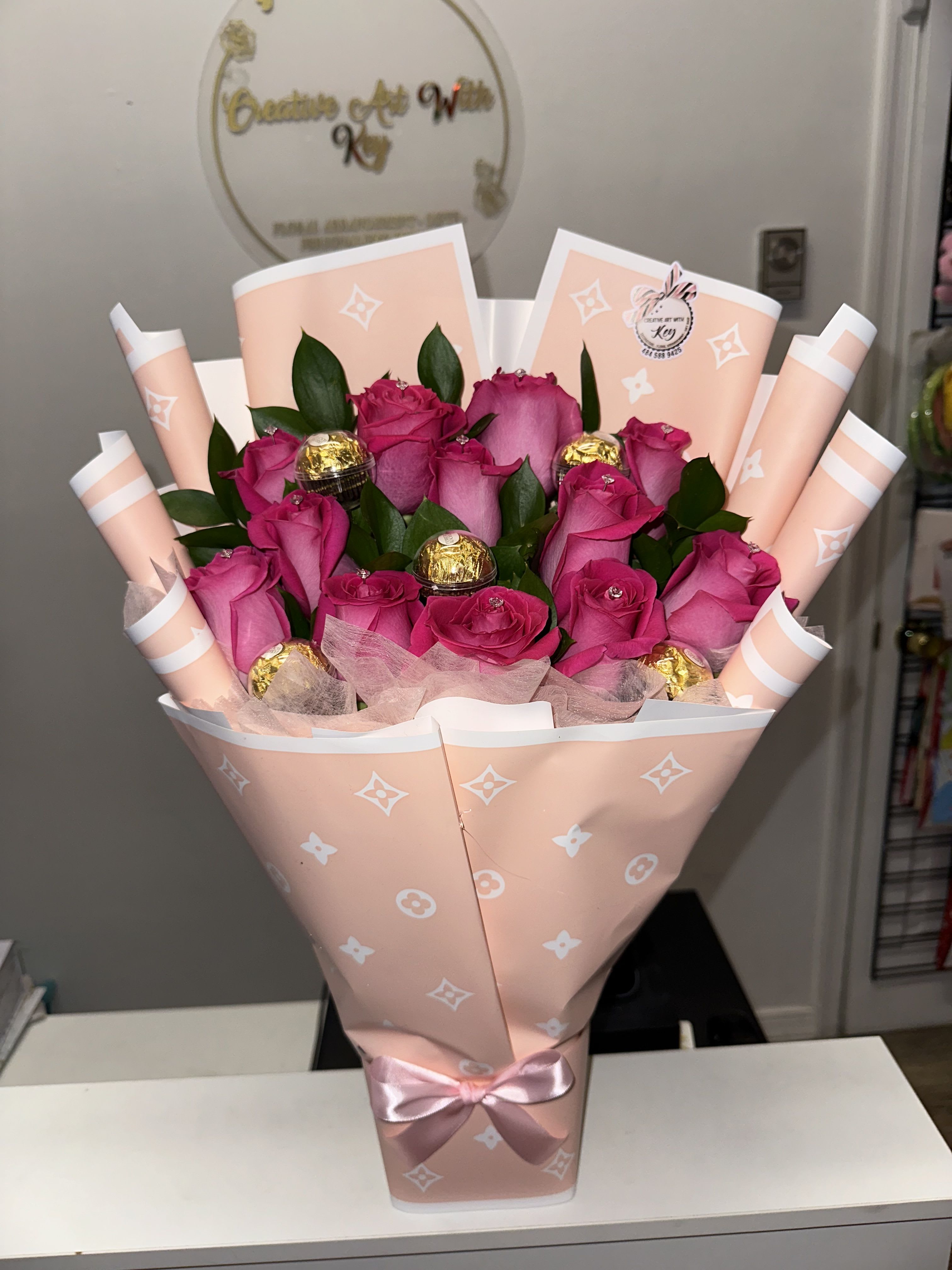 Pink rose bouquet wrapped in peach paper with a satin bow and chocolates