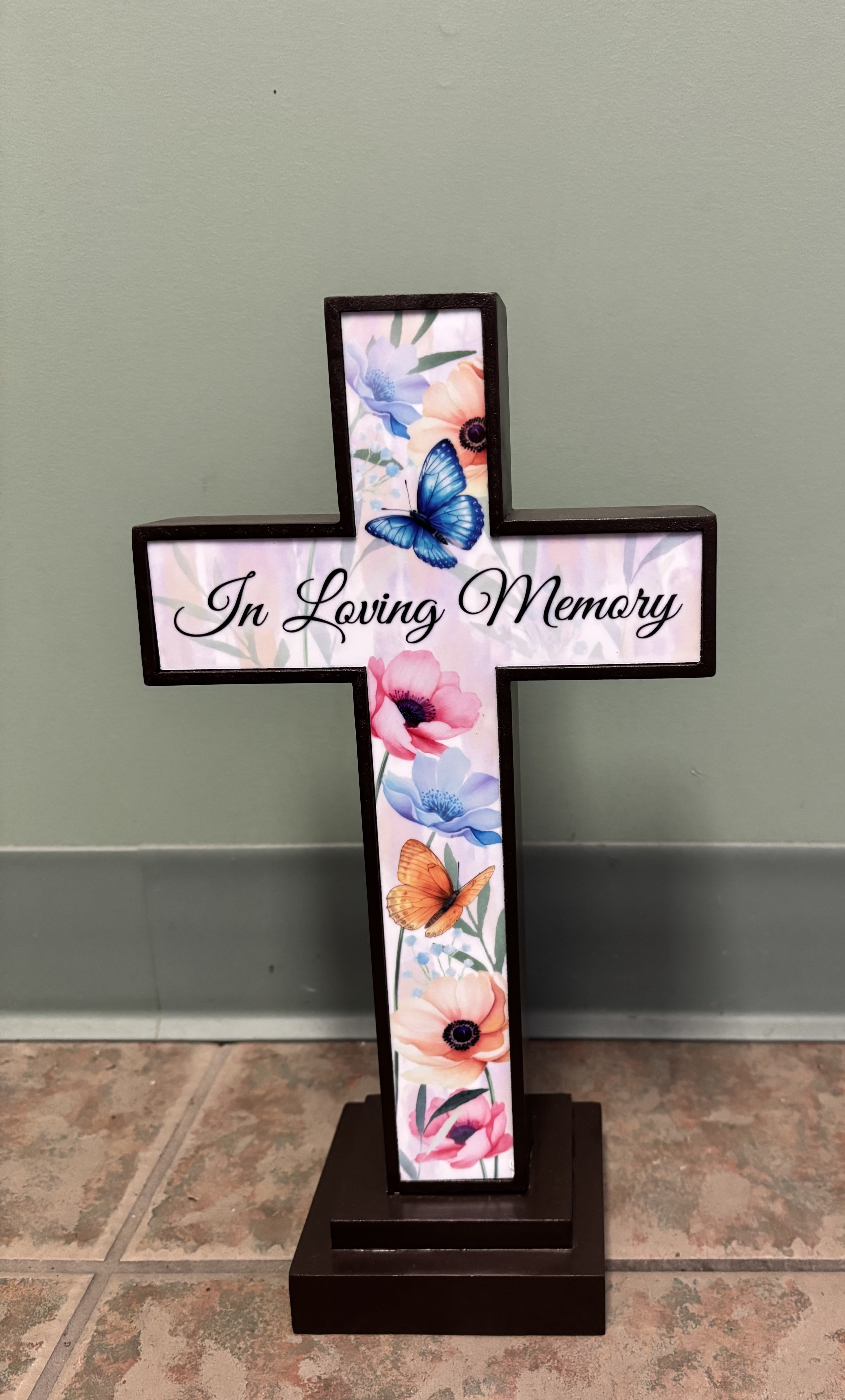Cross-shaped memorial sign with floral and butterfly artwork and the words In Loving Memory