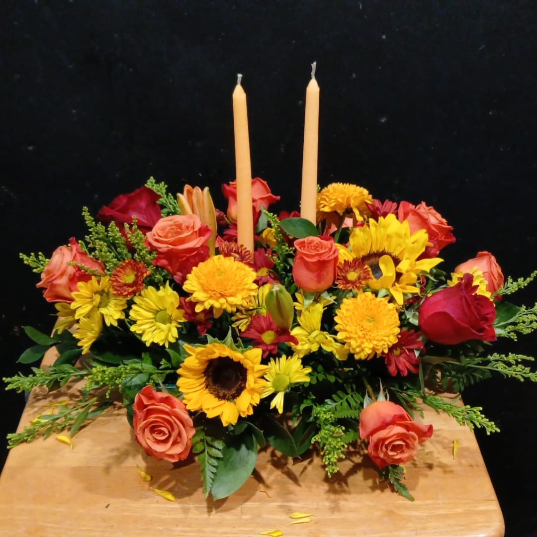 Floral centerpiece with roses, sunflowers, and two taper candles