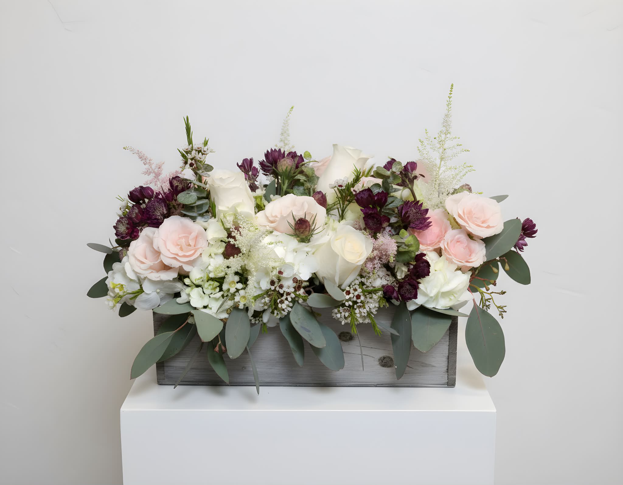 Winery vibes - This low, rectangular design is great for a centerpiece at a special occasion or any day you want to brighten someone’s day. The design comes in a wooden box and features a variety of foliage with delicate pink and white accents.