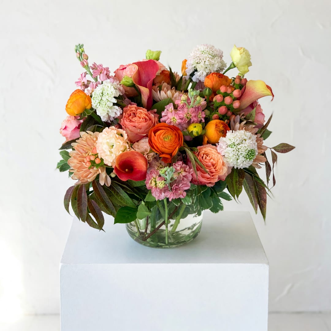 Mixed bouquet of orange, pink, and white flowers in a glass vase