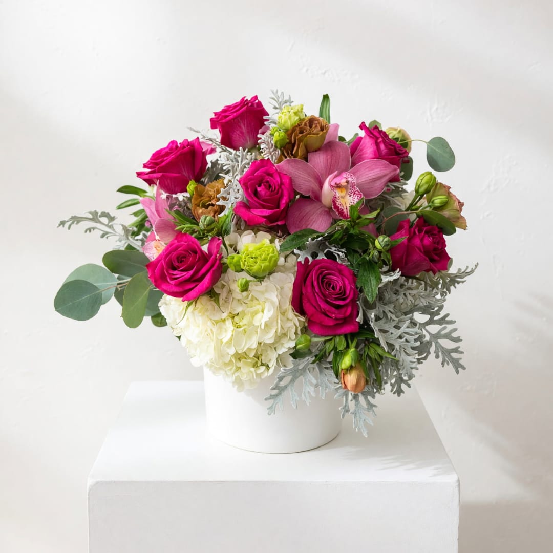 Pink roses and orchids arranged in a white vase.