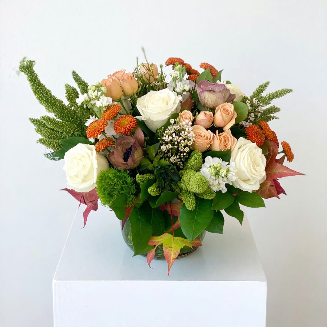 Mixed bouquet of roses and orange blooms in a glass vase