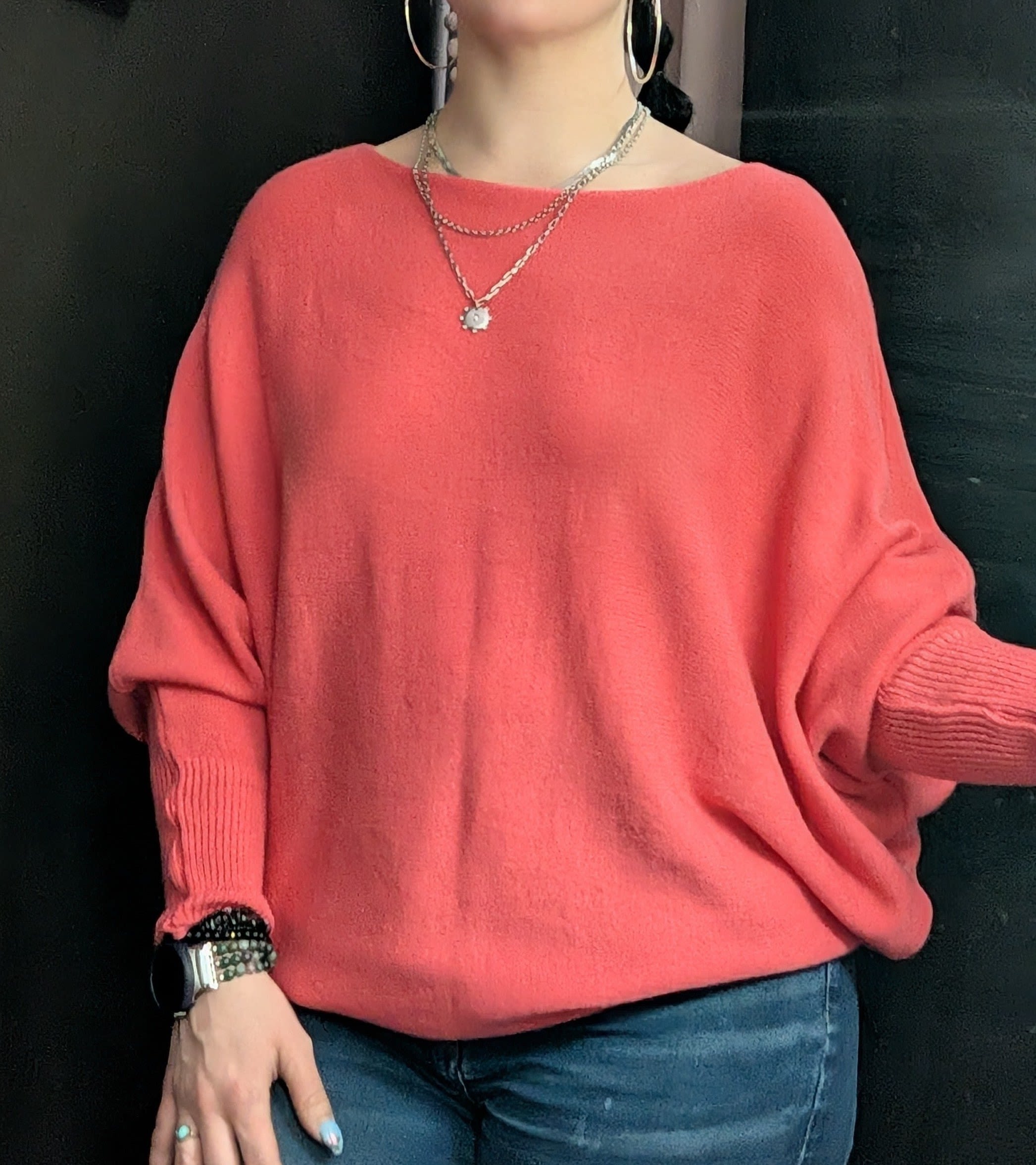Person wearing a coral oversized sweater with jeans and jewelry