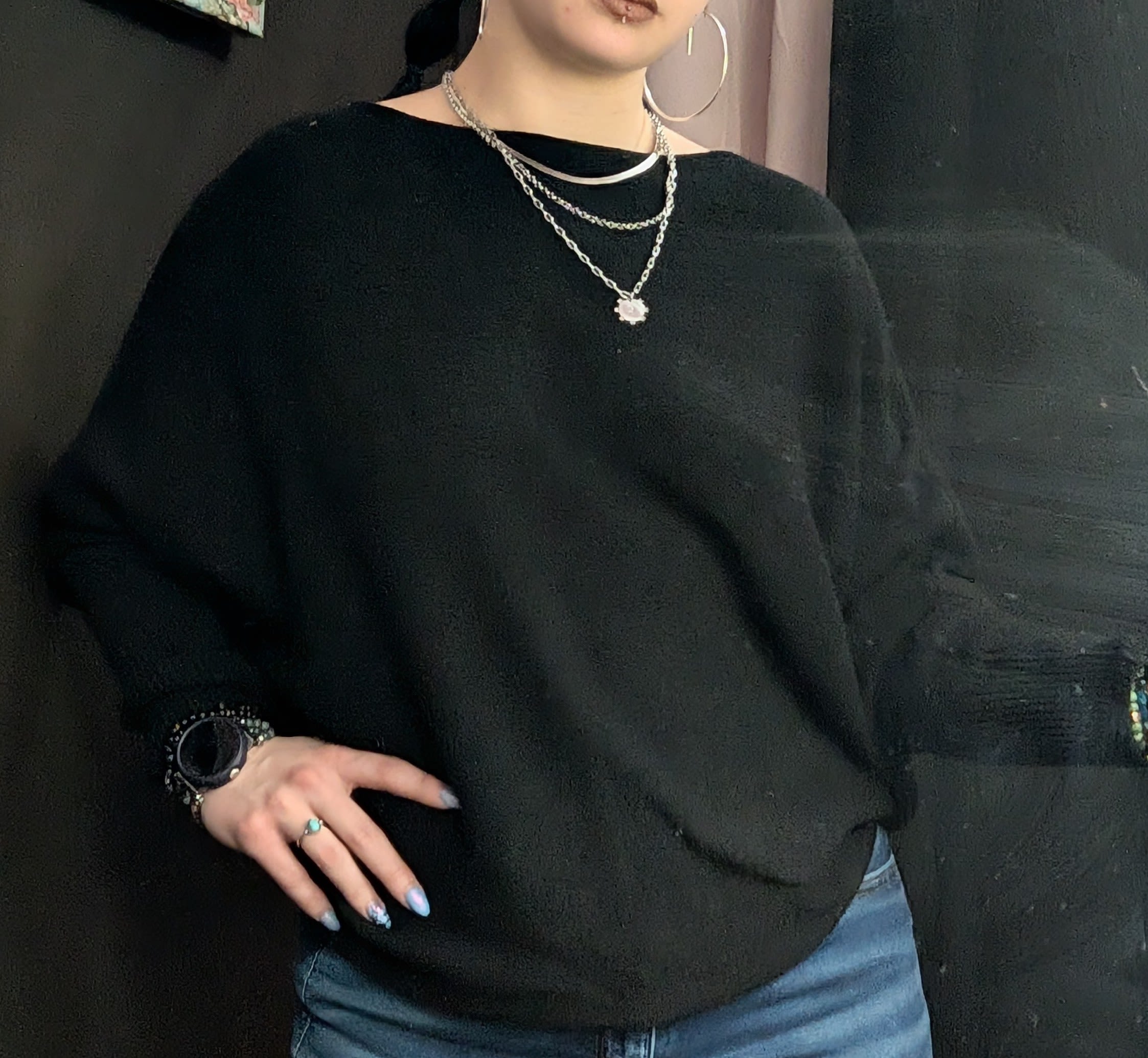 Person wearing a black sweater with layered silver necklaces and hoop earrings