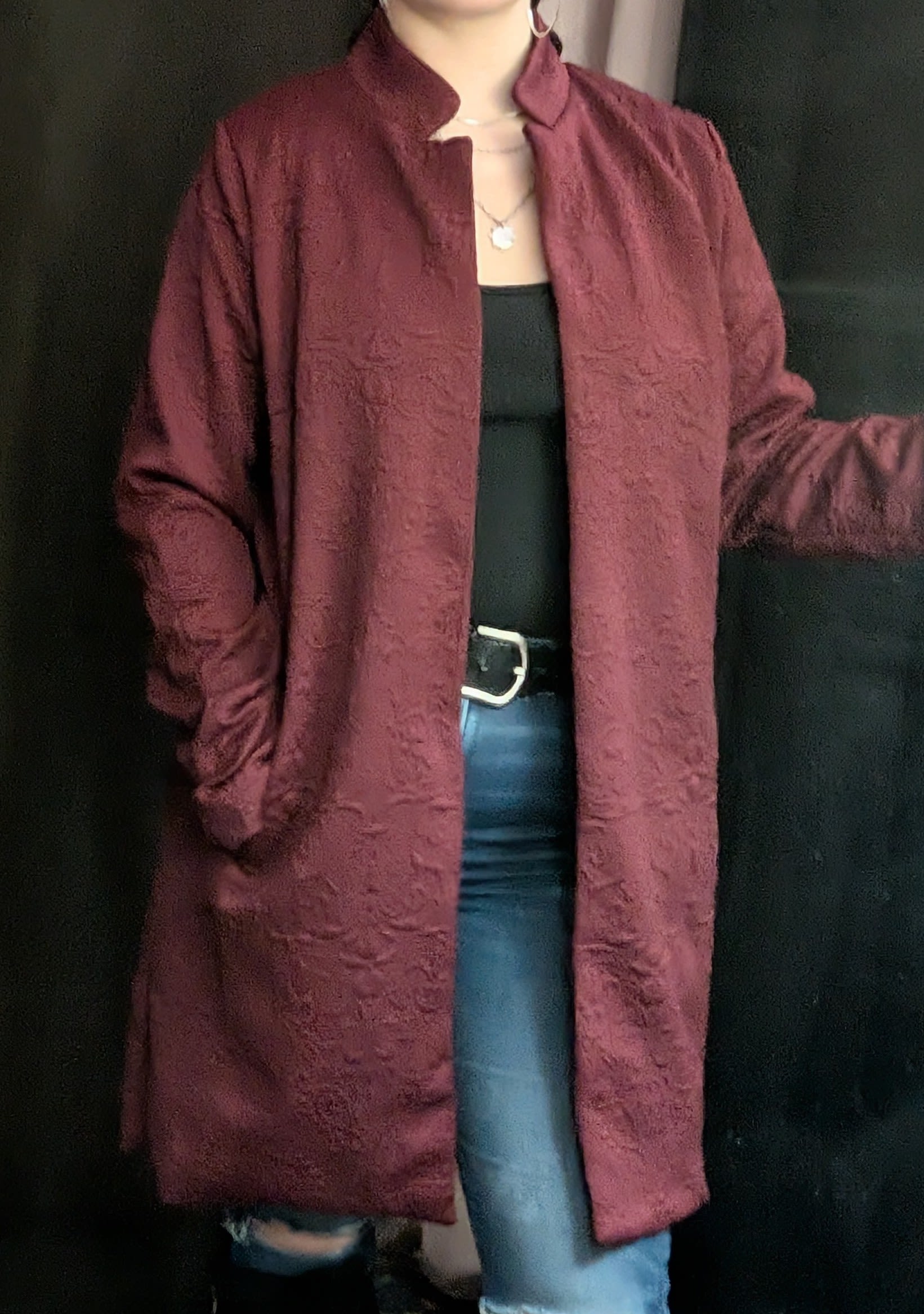 Person wearing a burgundy long coat over a black top and jeans