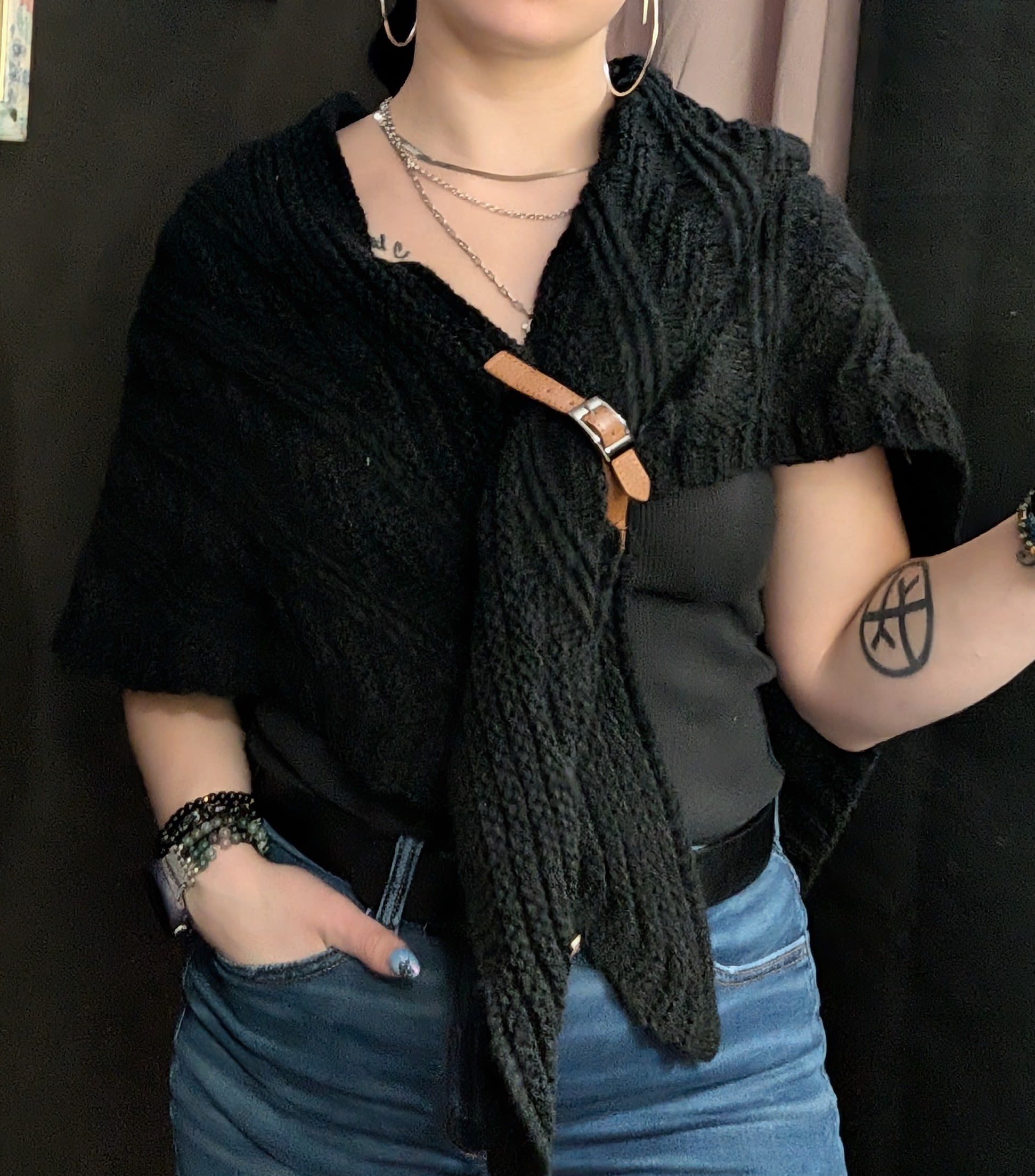 Person wearing a black textured top with a tan buckle detail and blue jeans