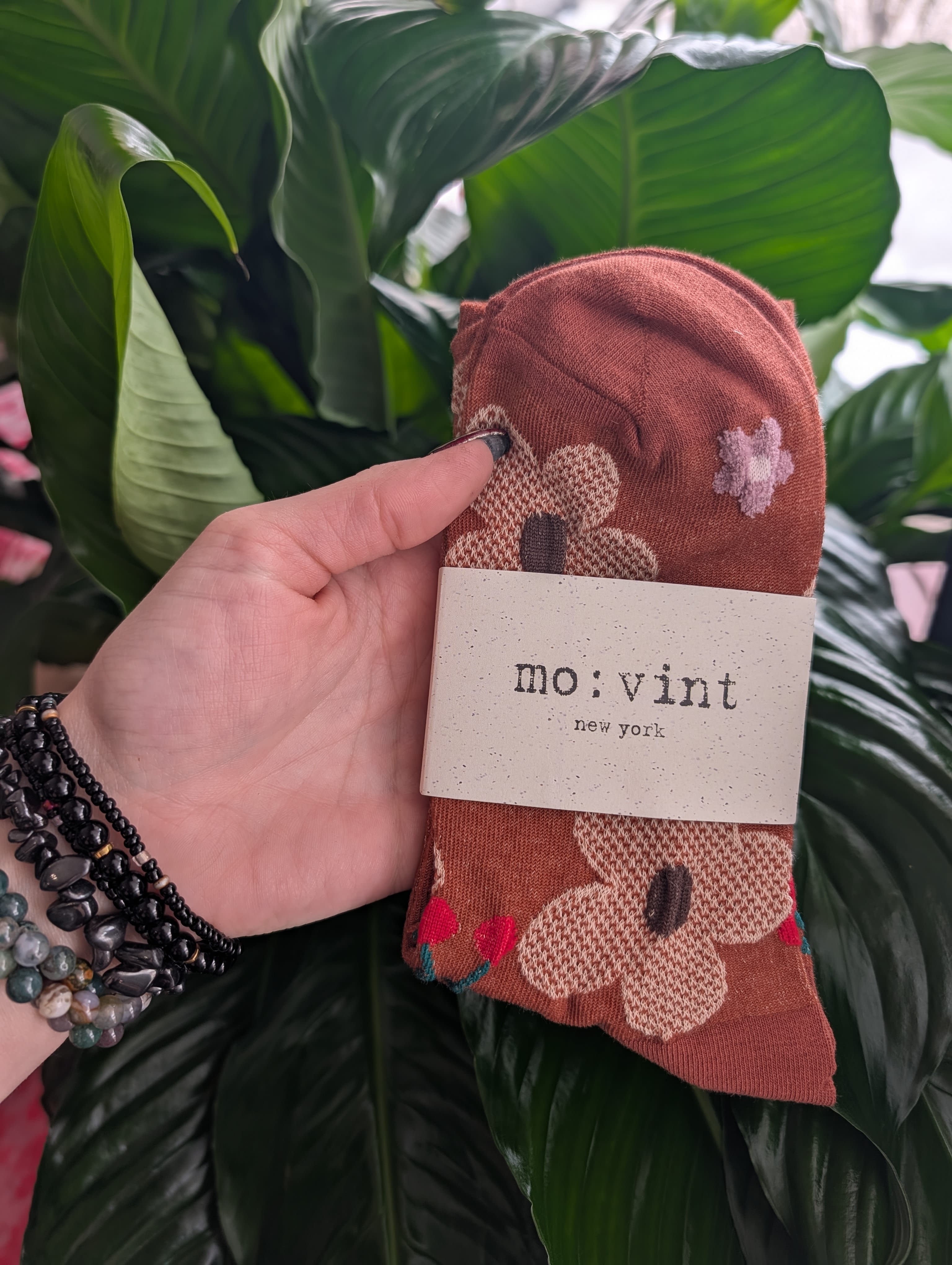 Hand holding folded patterned socks with a mo: vint label