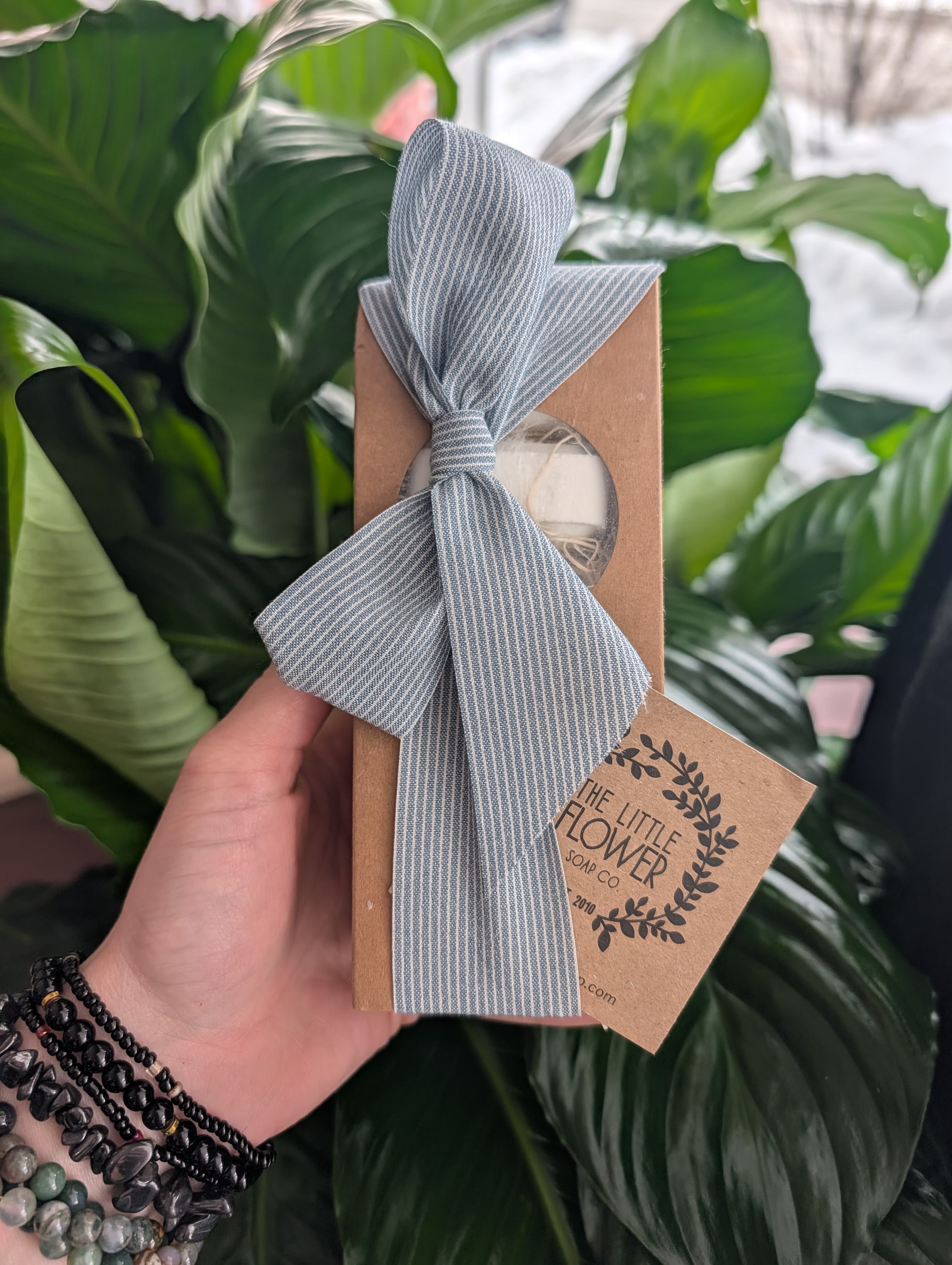 Handheld kraft soap box tied with a gray striped ribbon