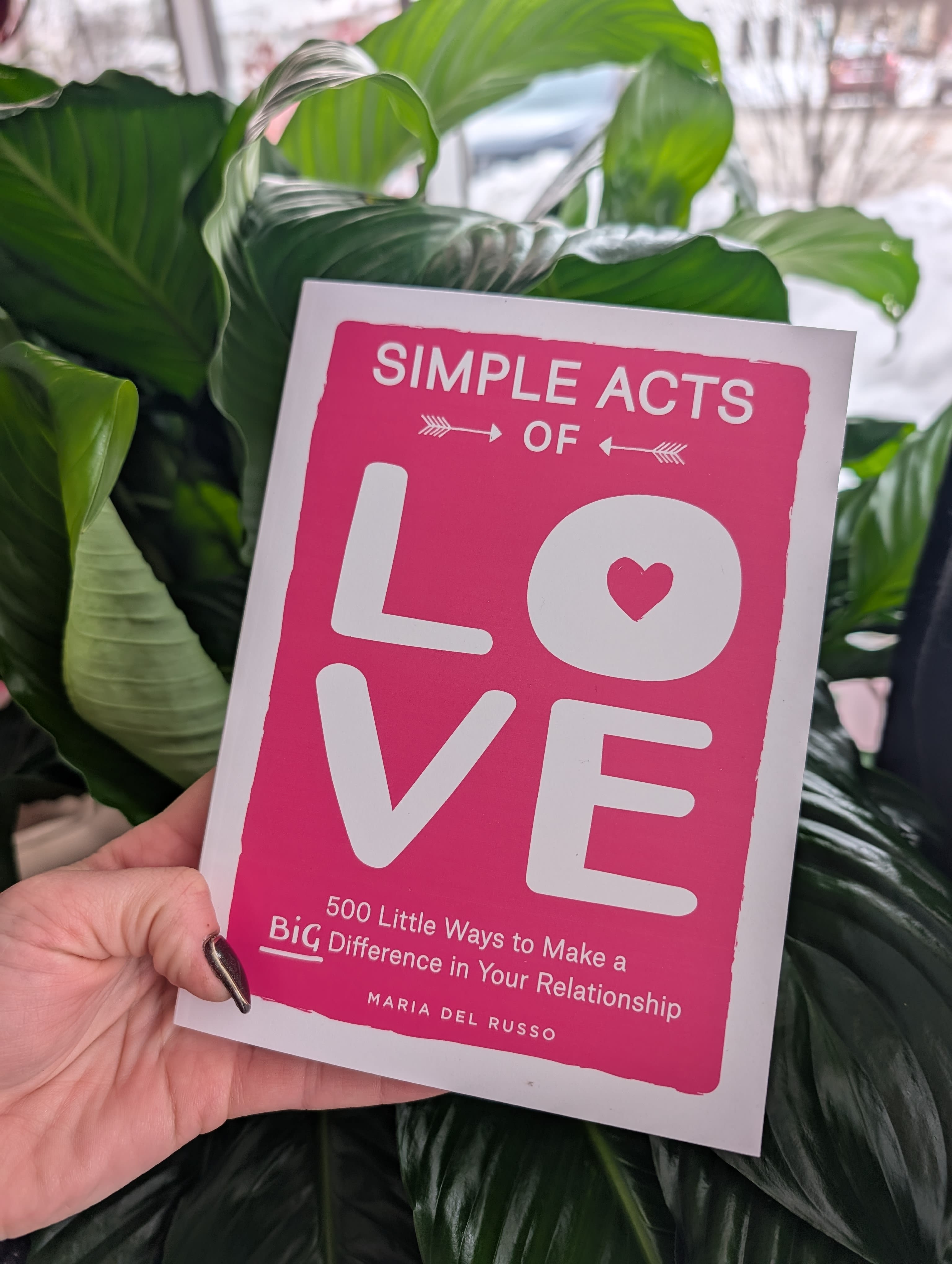 Hand holding a pink book cover reading "Simple Acts of Love"