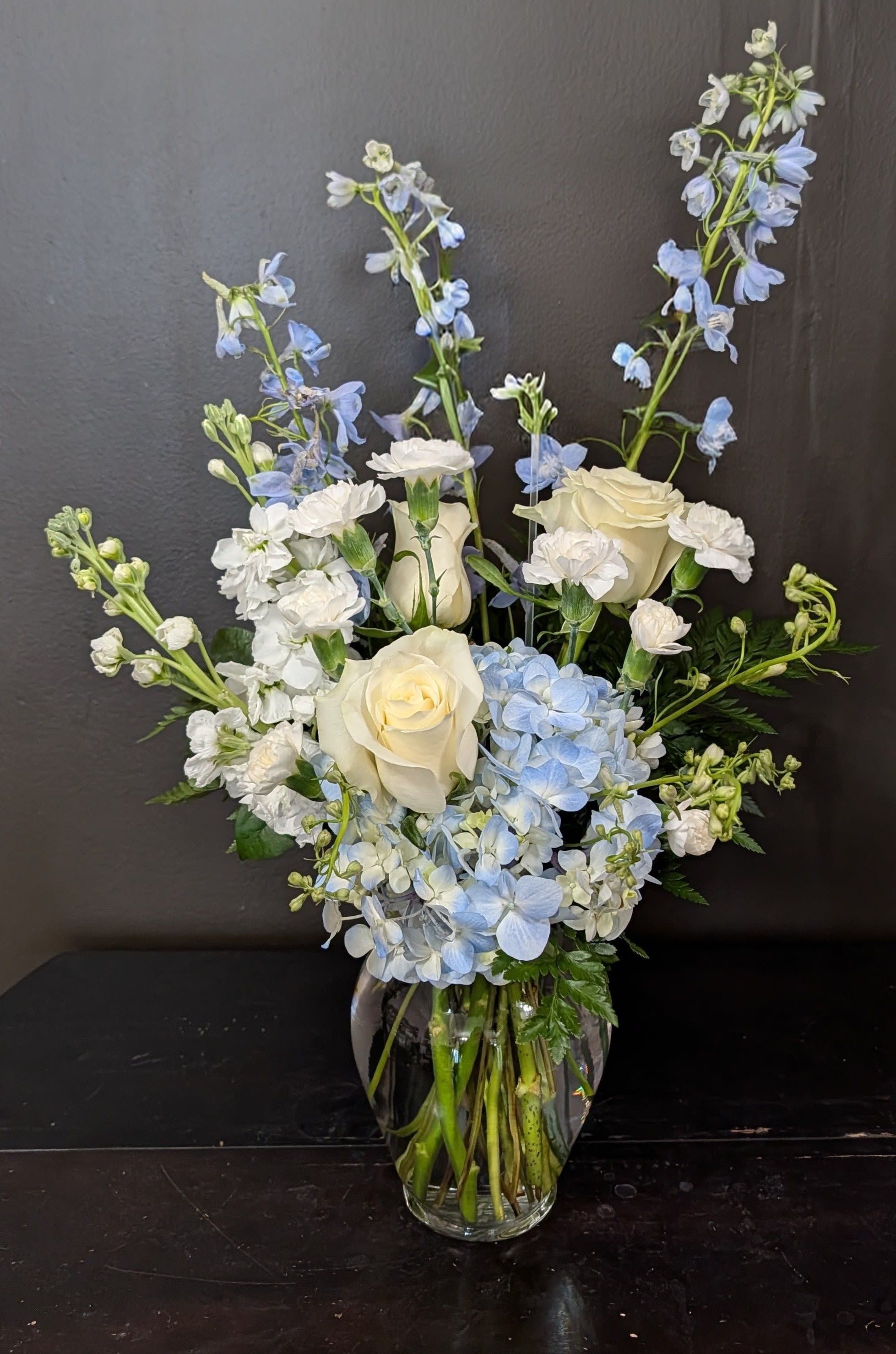 White roses and blue flowers arranged in a glass vase
