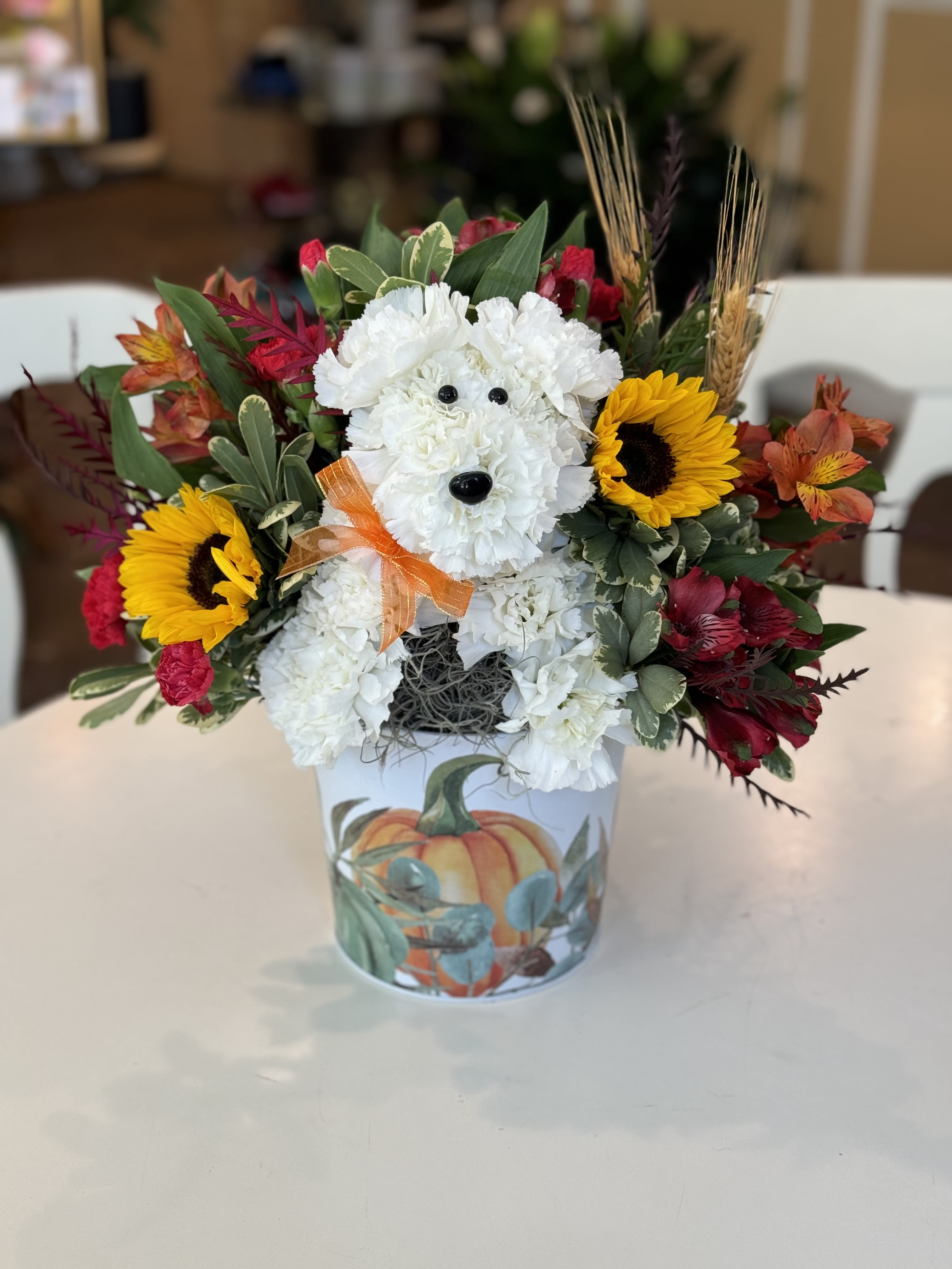 White floral dog arrangement in a pumpkin-decorated container with sunflowers