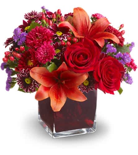 Red and orange floral arrangement in a square glass vase