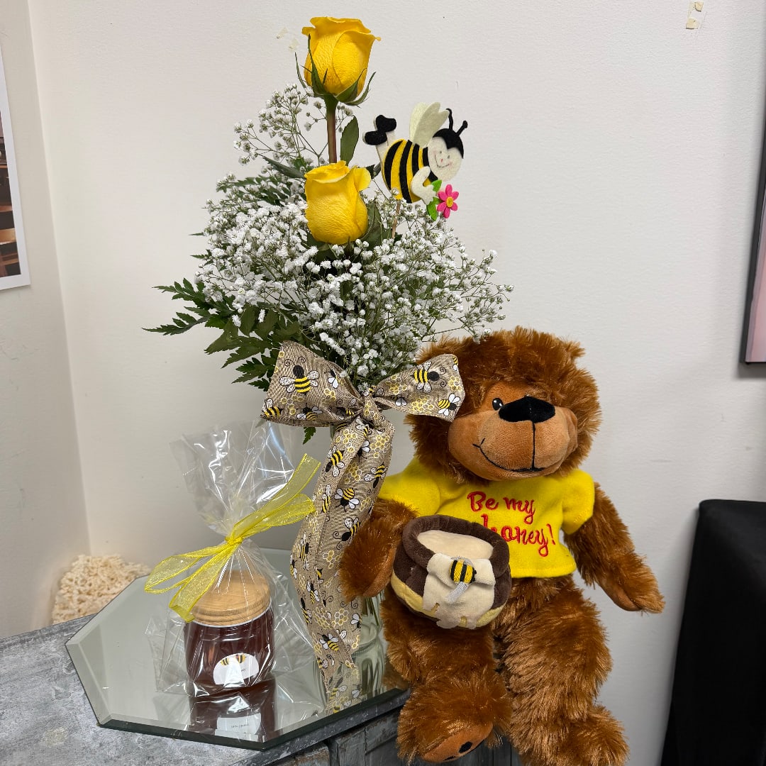 Yellow roses in a glass vase with a teddy bear and honey jar