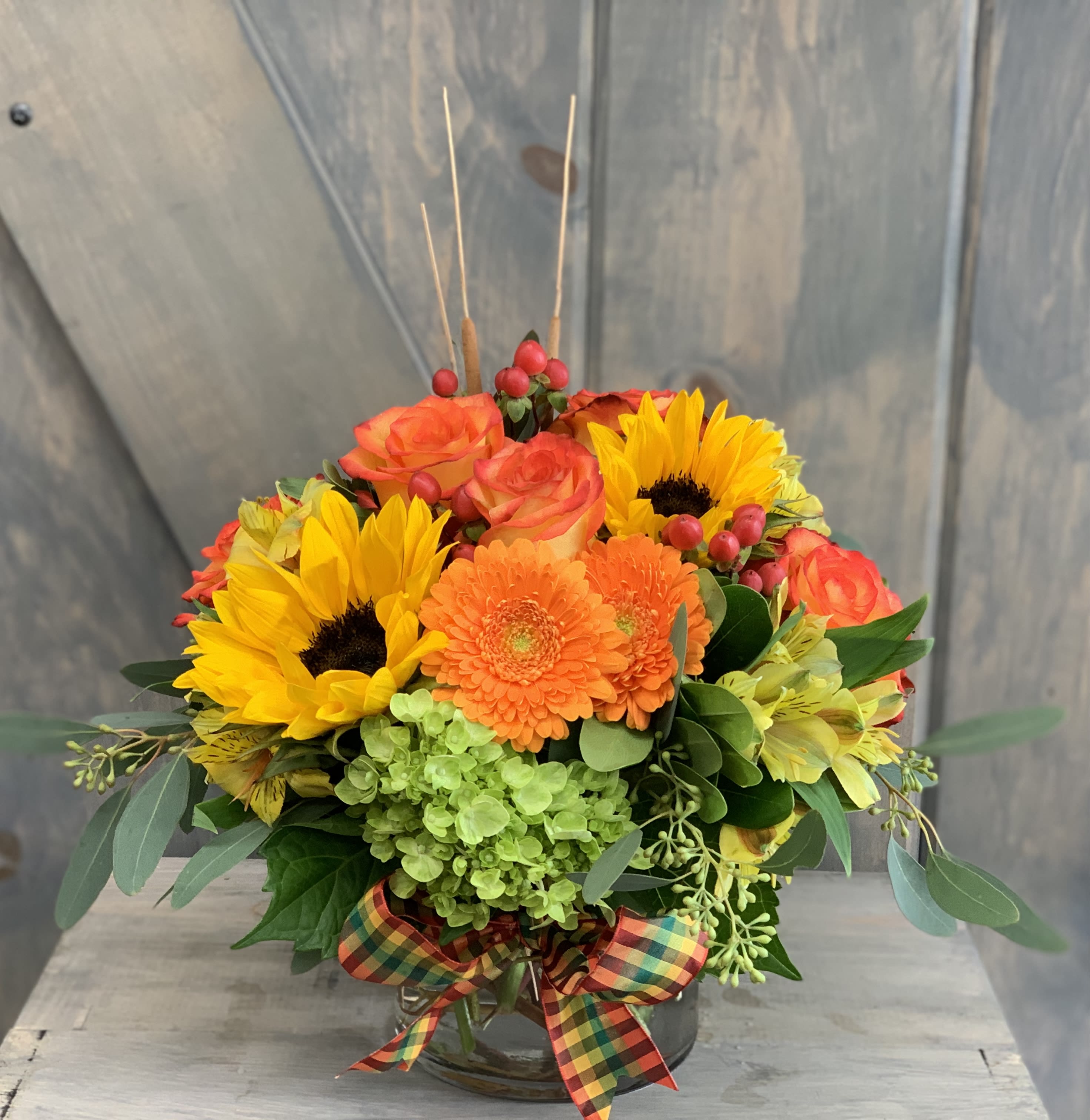Bright mixed bouquet with sunflowers, orange roses, and gerbera daisies in a glass vase