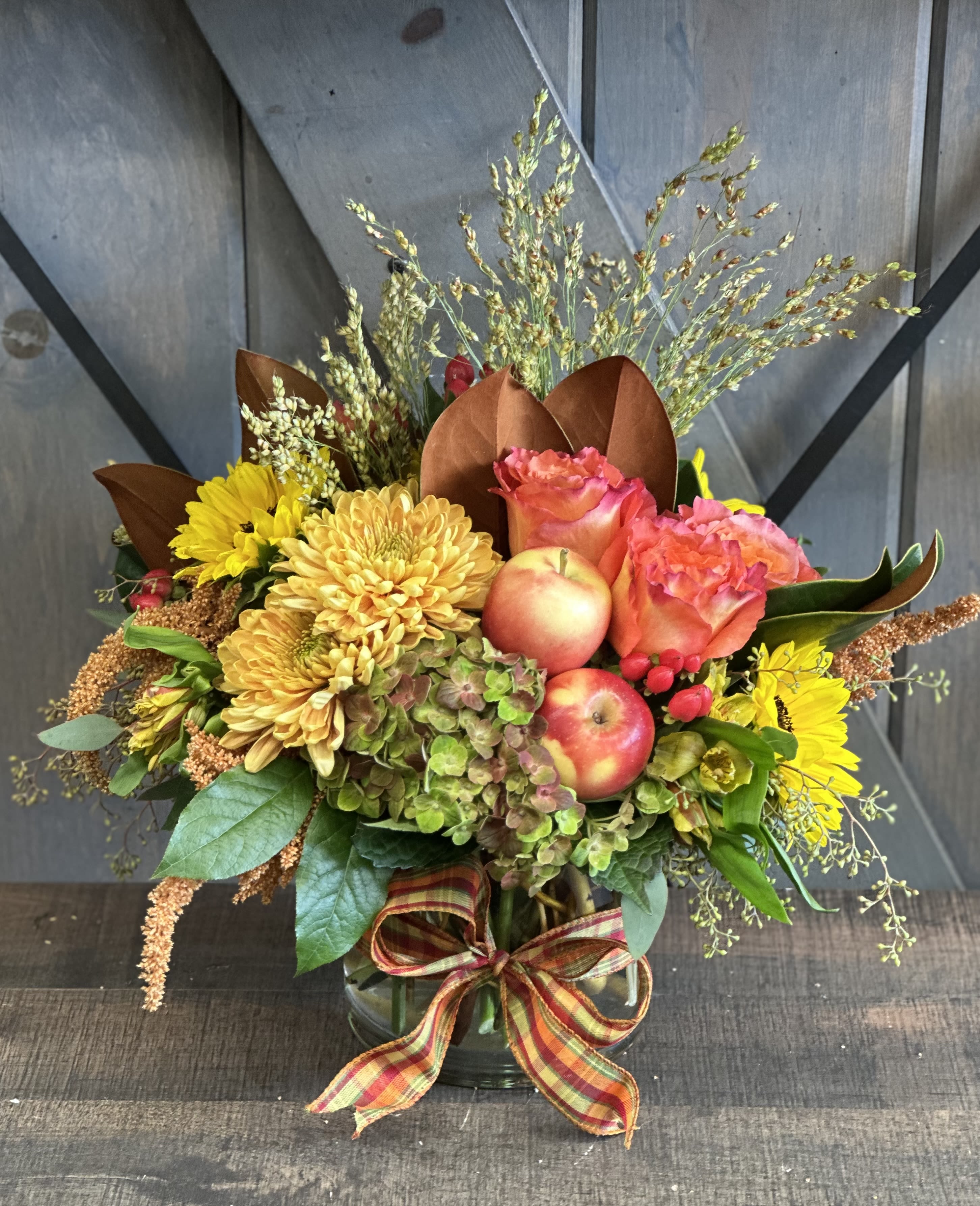 Autumn bouquet with yellow chrysanthemums, pink roses, and apples in a glass vase
