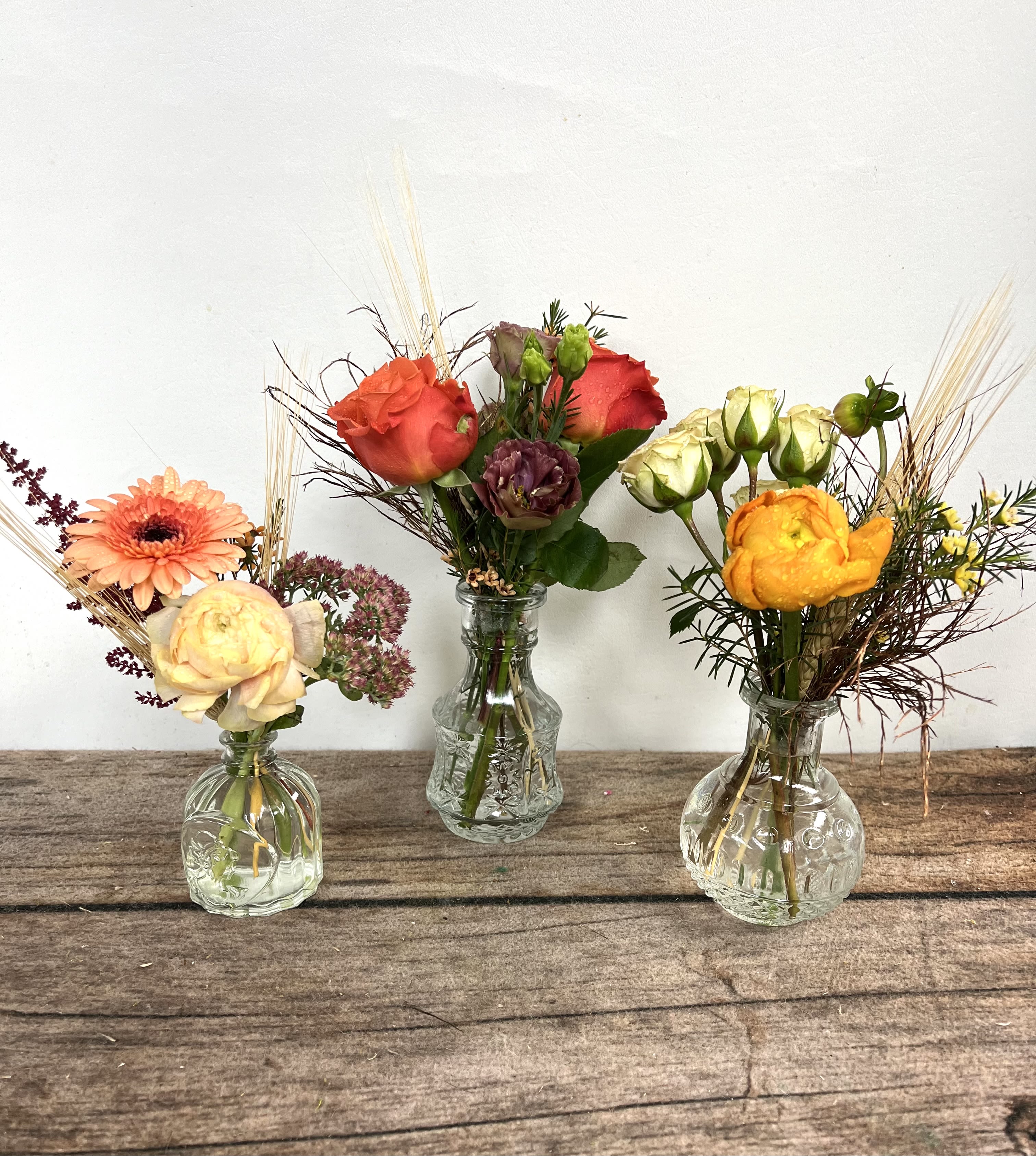 Three small flower arrangements in clear glass vases on a wooden surface