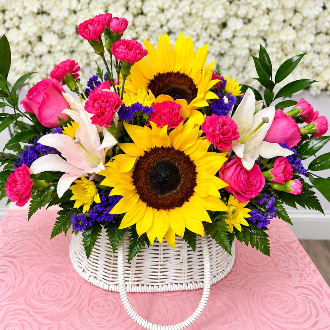 Bright bouquet with sunflowers, pink carnations, and white lilies in a white basket
