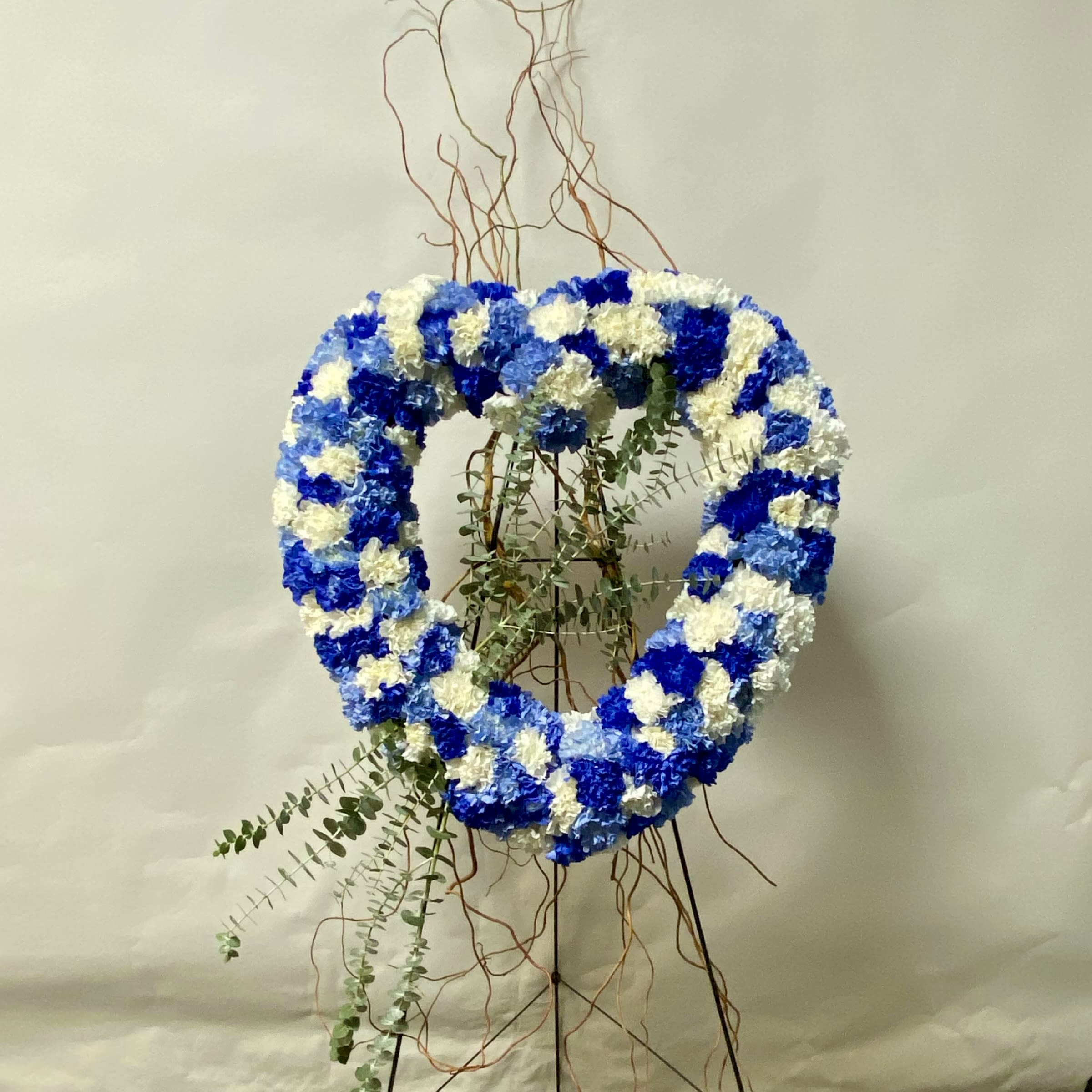 Blue Horizon Open Heart - This Standing Open Heart Includes White, Light Blue and Royal Blue Carnations Accented with Branches and Greenery. Or as Similar as Possible. 