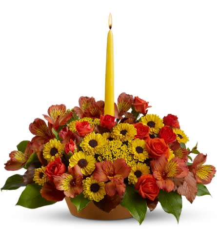 Yellow candle in a low arrangement of red and yellow flowers