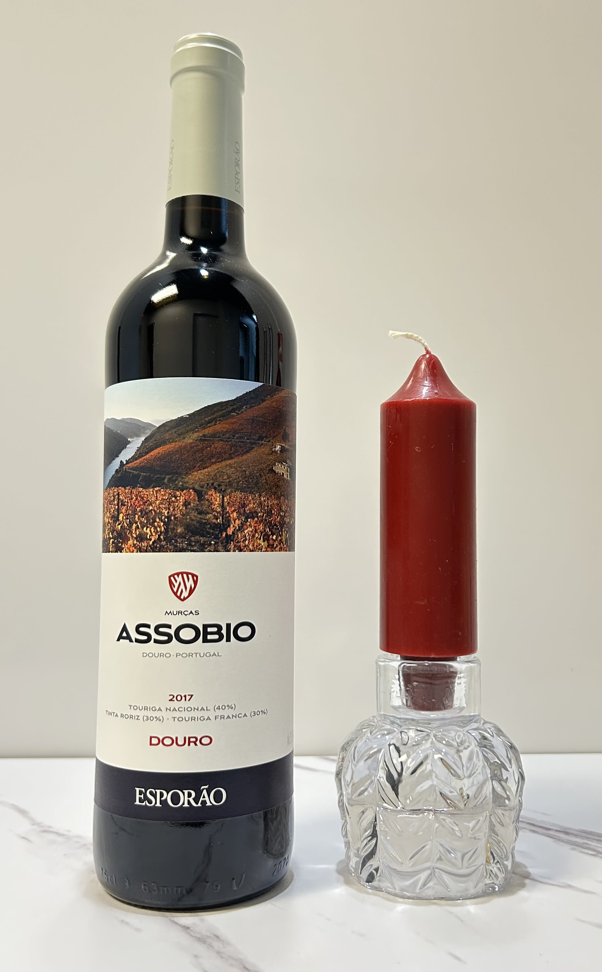 Wine bottle beside a red candle in a clear glass holder