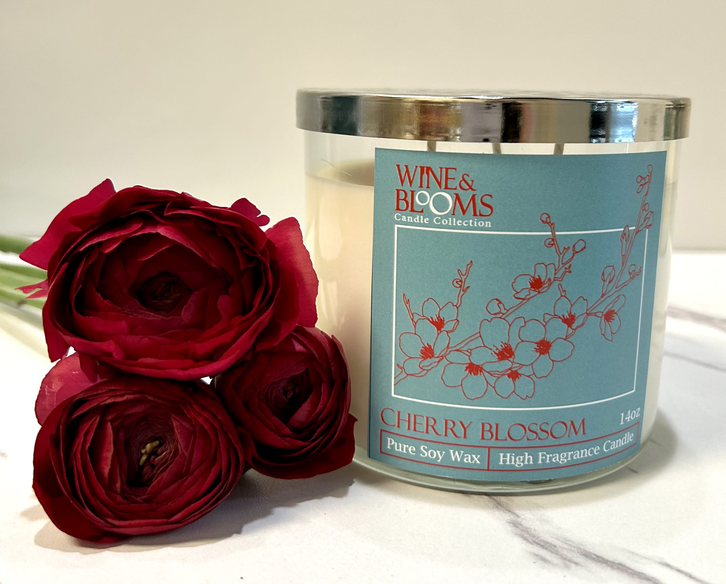Red roses beside a cherry blossom candle in a glass jar
