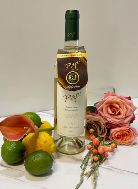 Wine bottle with roses, citrus, and a calla lily on a white surface