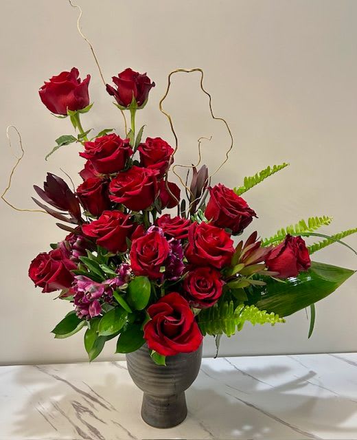 Red roses arranged in a dark vase with green foliage