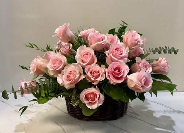 Pink roses arranged in a dark basket with greenery
