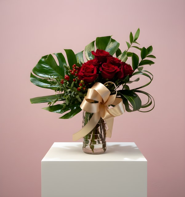 Arrangement of red roses with large glossy leaves in a glass vase tied with a gold bow