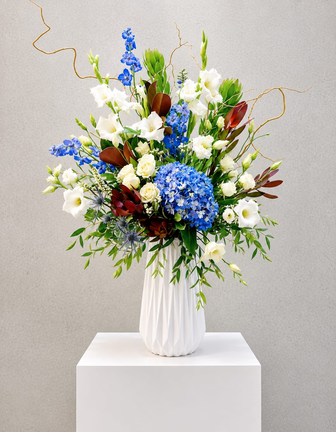 Tall floral arrangement with blue and white blooms in a white vase