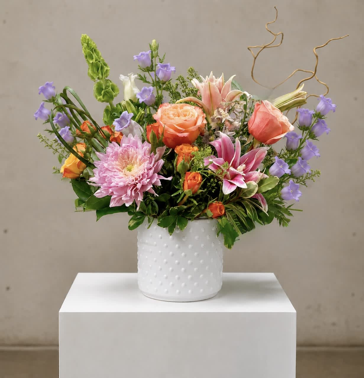 Mixed bouquet of pink, peach, purple, and white flowers in a white vase