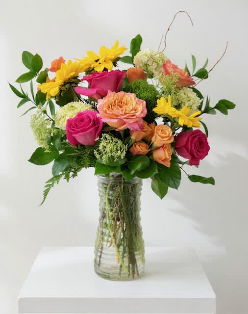Mixed bouquet of pink, peach, and yellow flowers in a clear glass vase