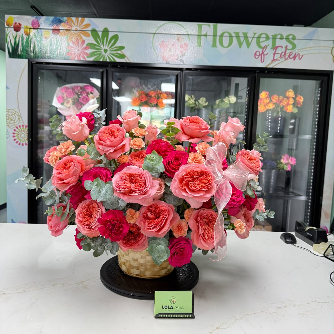Pink and coral rose arrangement in a woven basket with a ribbon bow.