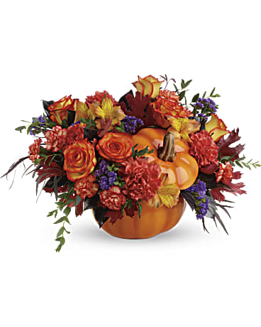 Autumn floral arrangement in a pumpkin container with orange and red blooms