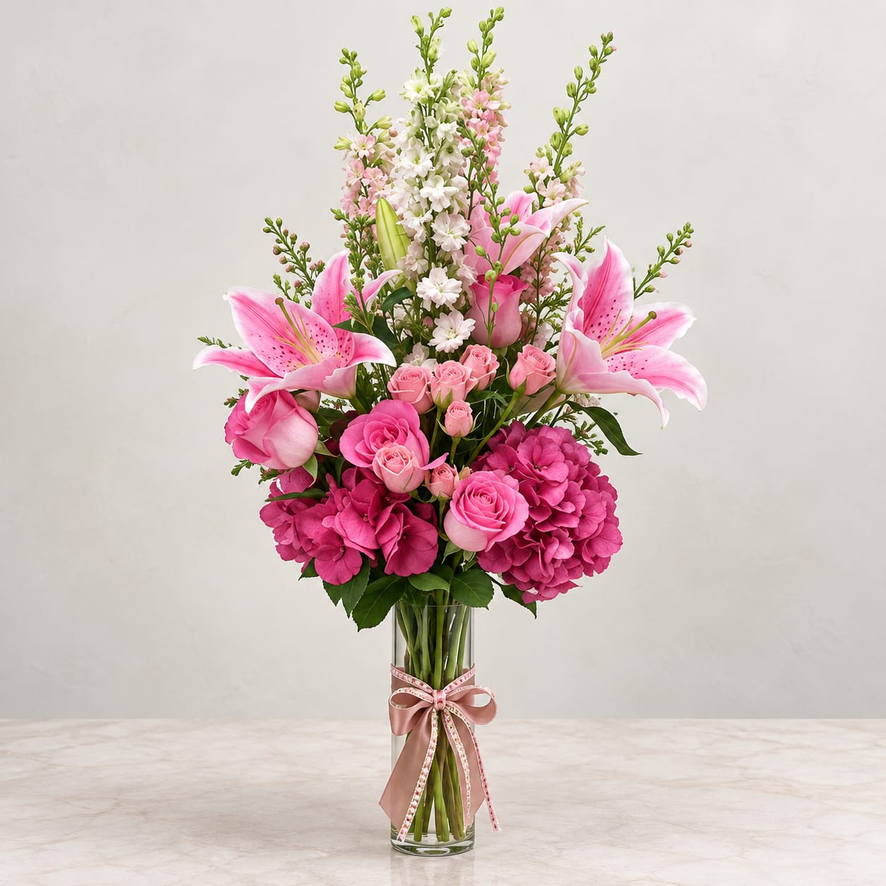 Pink lilies and roses in a clear glass vase with a ribbon