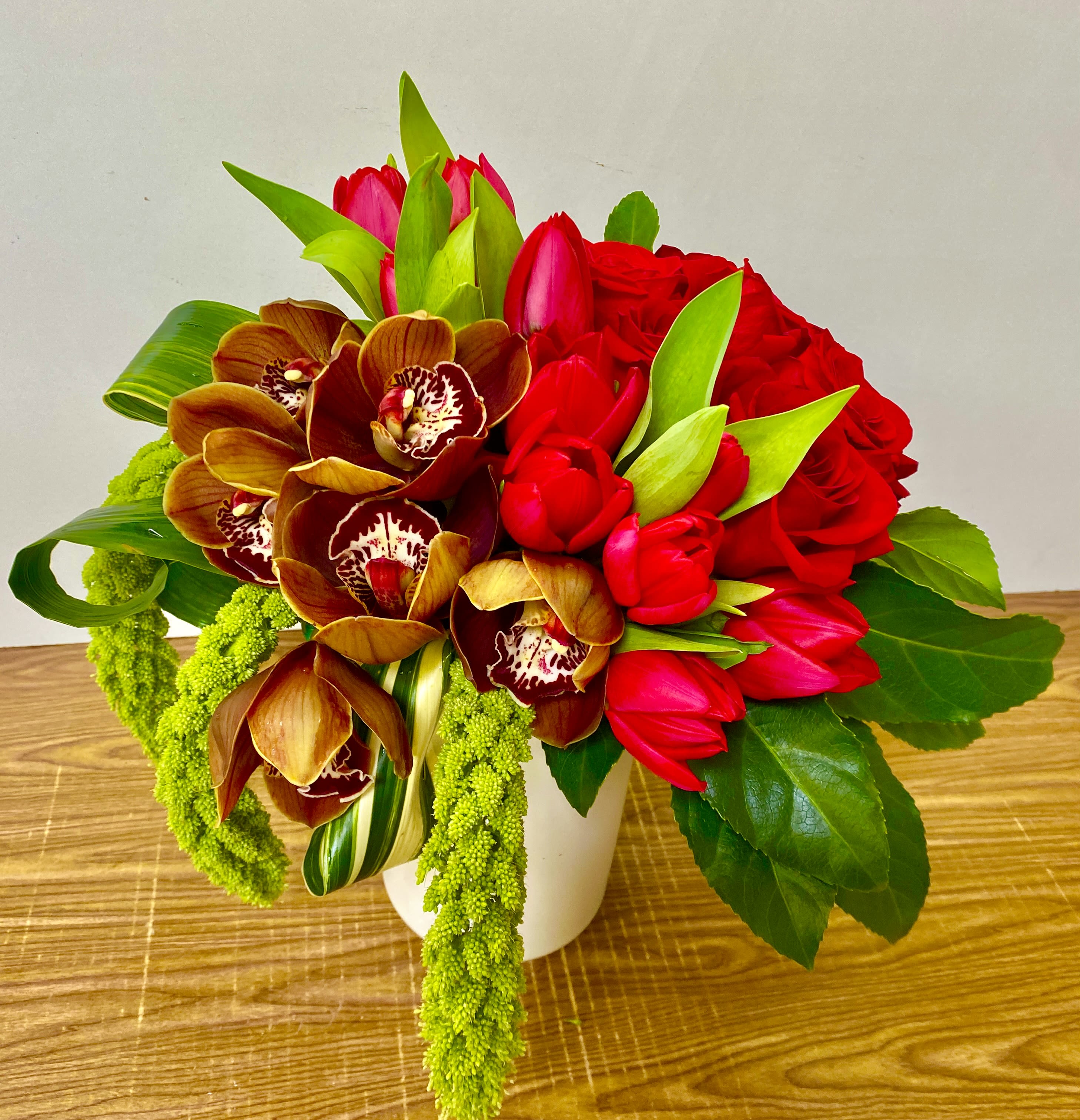 Bouquet of red roses, red tulips, and orchids in a white vase