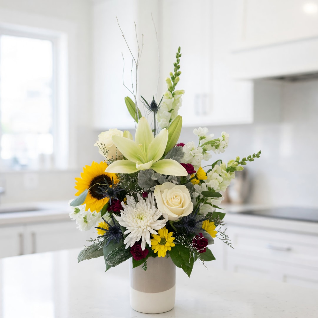 Mixed bouquet in a ceramic vase with a lily, sunflower, and white blooms