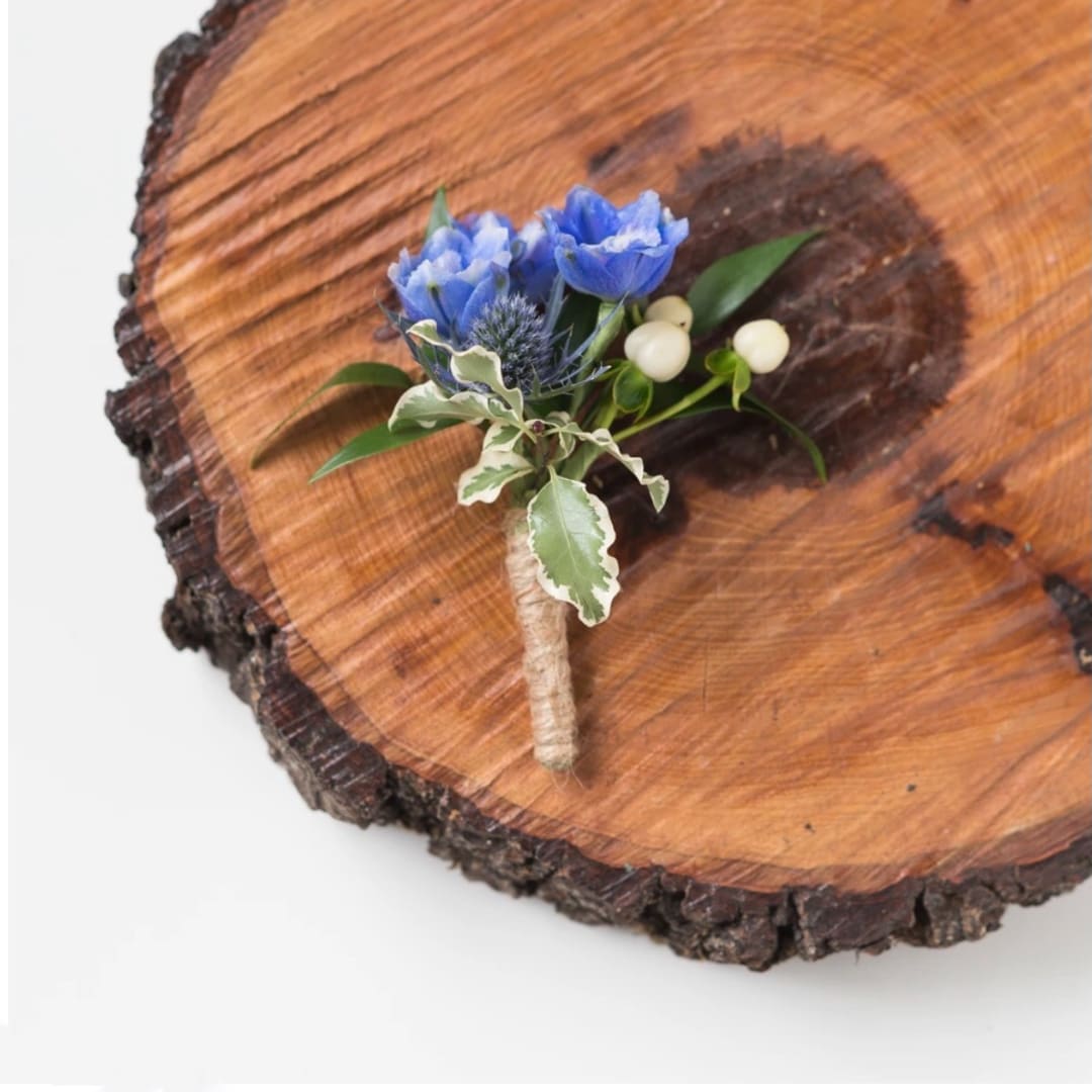Blue boutonniere with white berries on a wood slice