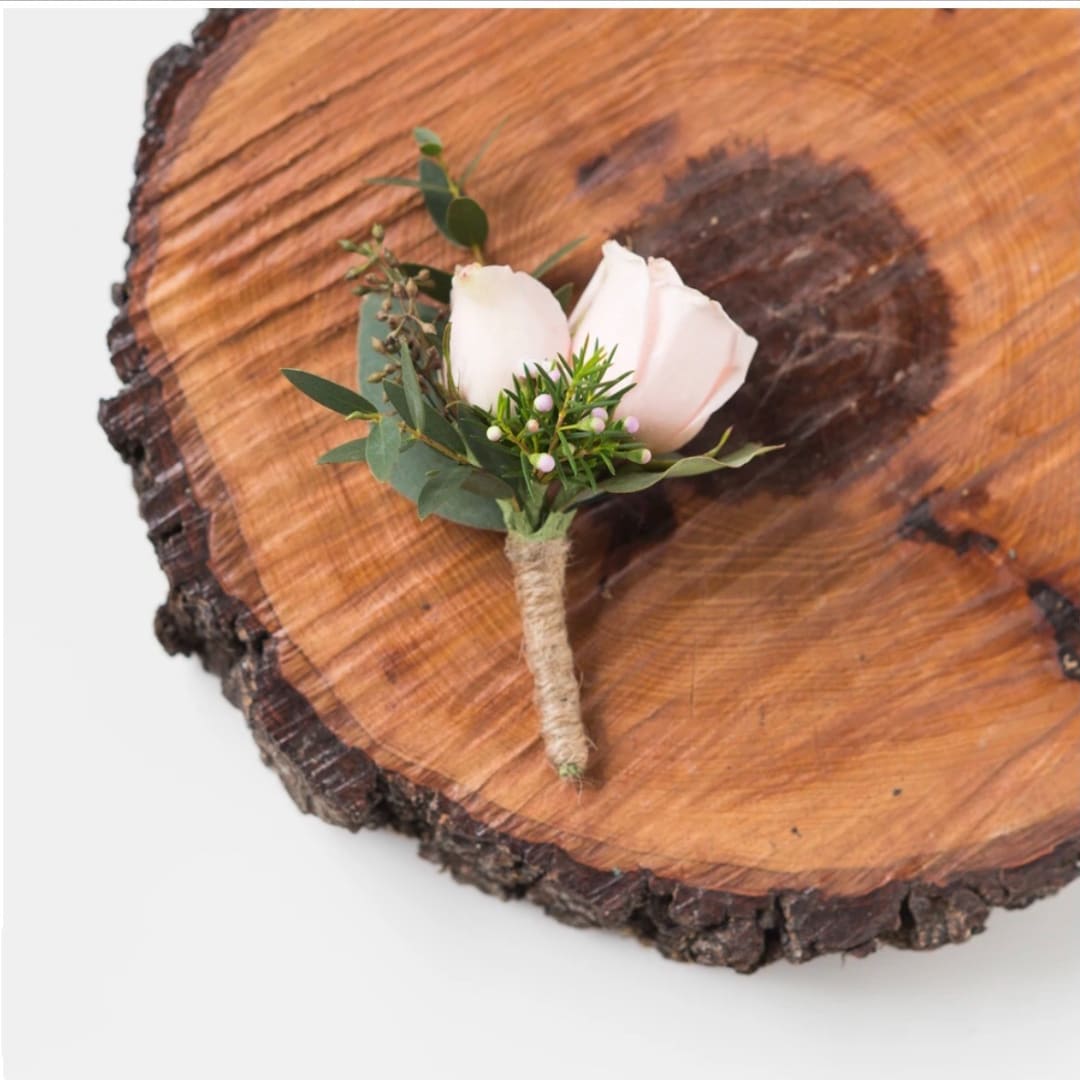 White rose boutonniere with greenery on a wood slice