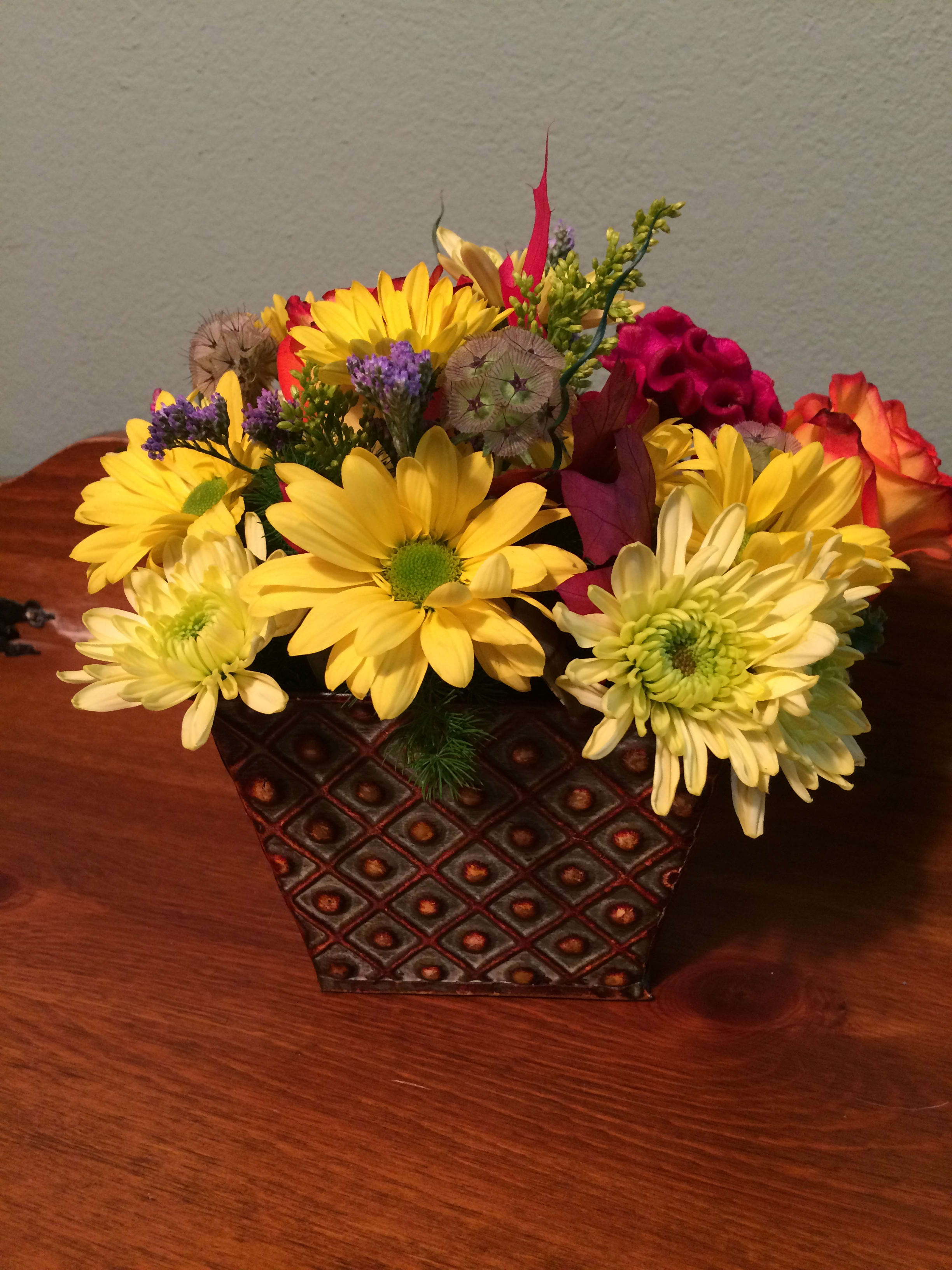 Yellow daisies and mixed flowers arranged in a patterned square container