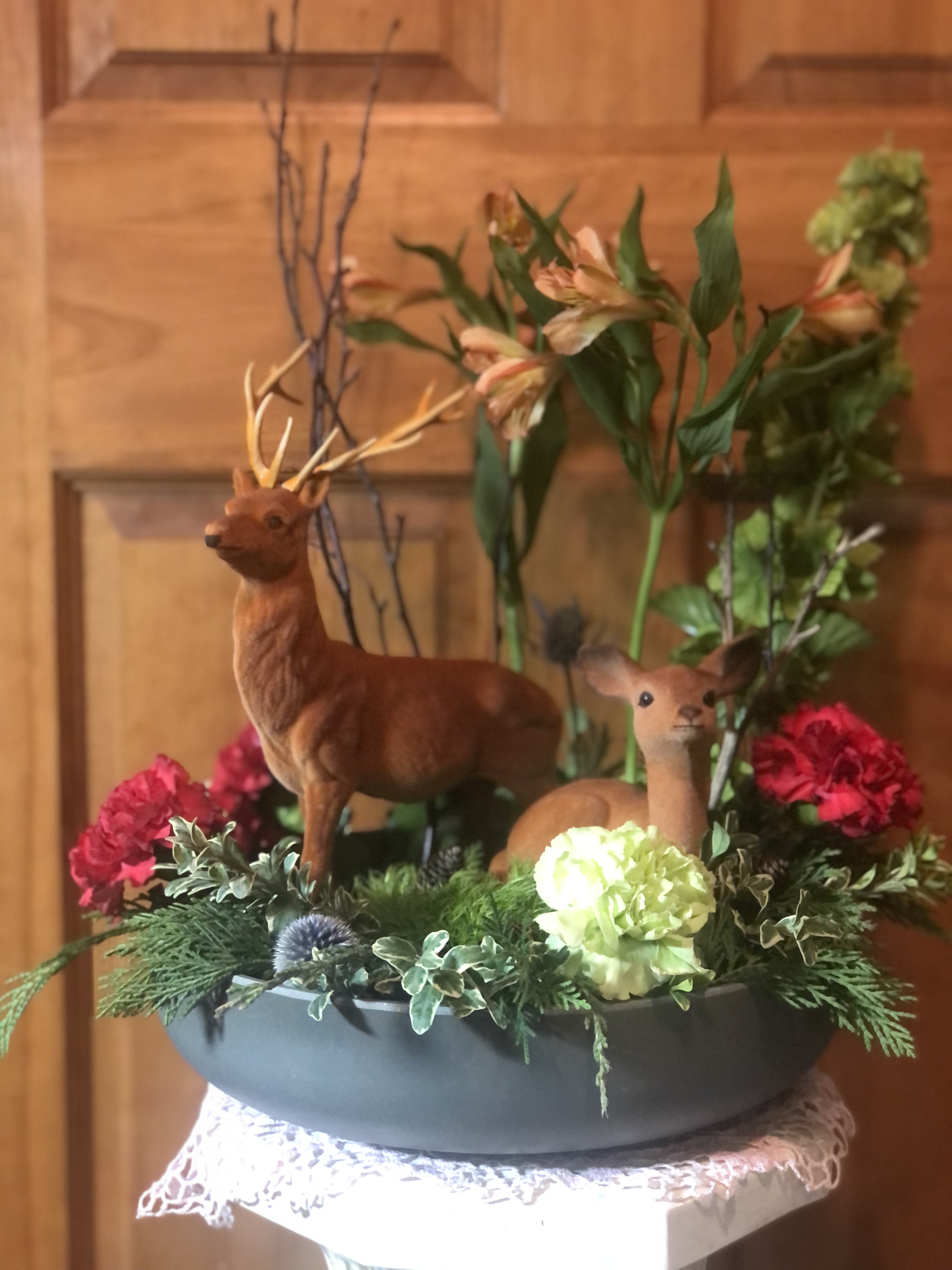 Floral arrangement with deer figurines in a low gray container