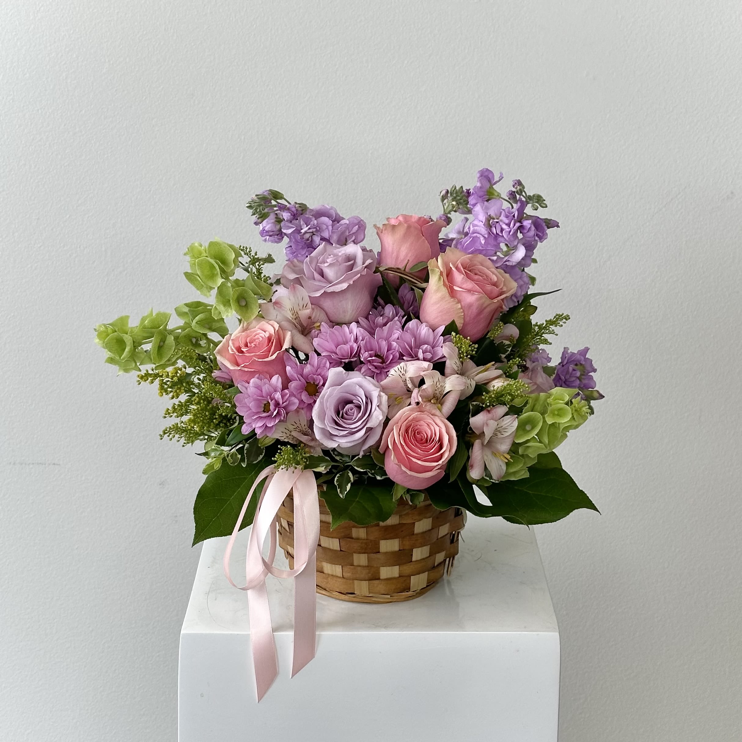 Basket of Love - Overflowing with meadow magic, the “Basket of Love” is a whimsical wildflower dream in a rustic woven basket! Lavender roses mingle with airy larkspur, lavender &amp; white daisies dance alongside purple &amp; green cushion pompons, while delicate wax flower, silver dollar eucalyptus, ruffled lisianthus, and starry Aster Matsumoto create untamed romance. This garden-picked bounty evokes carefree fields and heartfelt affection.  Why You’ll Fall for Basket of Love: Lavender Roses: Enchanting symbols of love at first sight and enchantment. Larkspur: Tall spires in purple add height and playful drama. Lavender &amp; White Daisies: Innocent, cheerful blooms for pure joy. Purple &amp; Green Cushions: Fluffy pompons bring texture and fun. Wax Flower: Tiny starry clusters for delicate filler. Lisianthus: Rose-like ruffles in soft hues for sophistication. Aster Matsumoto: Star-shaped accents sparkle like wildflower confetti.  Hand-arranged in a natural woven basket with handle—perfect for picnics, porch displays, or gifting. Ideal for birthdays, thank yous, new babies, or “just because” love notes. Basket of love flowers, whimsical wildflower basket, larkspur lisianthus arrangement, woven basket floral delivery, rustic wildflower gift, birthday basket flowers, baby shower wildflowers, same-day whimsical bouquet. Capture wildhearted charm and order “Basket of Love” now! Same day delivery available.  Flowers are subject to substitution.