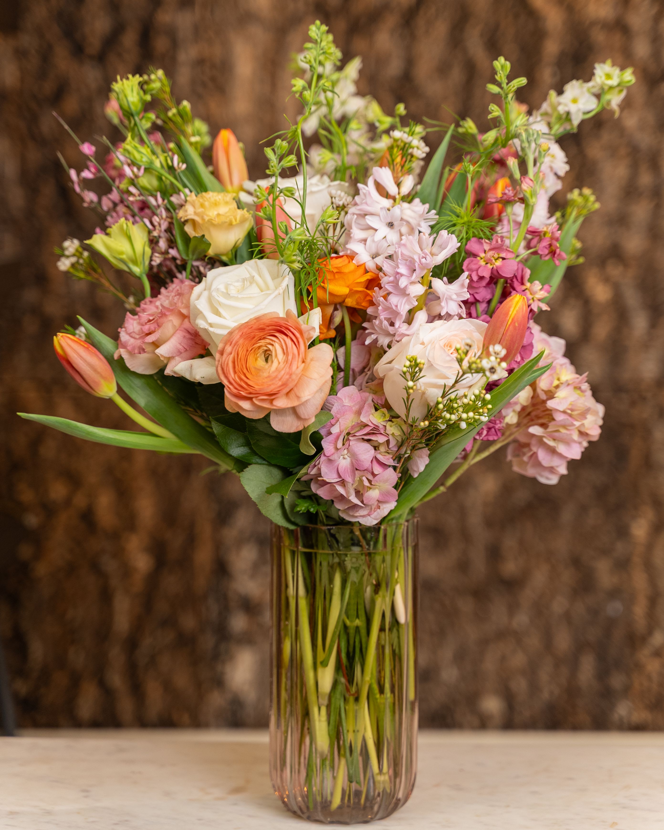 Tall mixed bouquet of pink, peach, and white flowers in a clear glass vase.