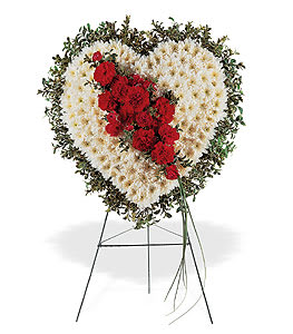 Heart-shaped white floral wreath with red flowers on a metal easel stand