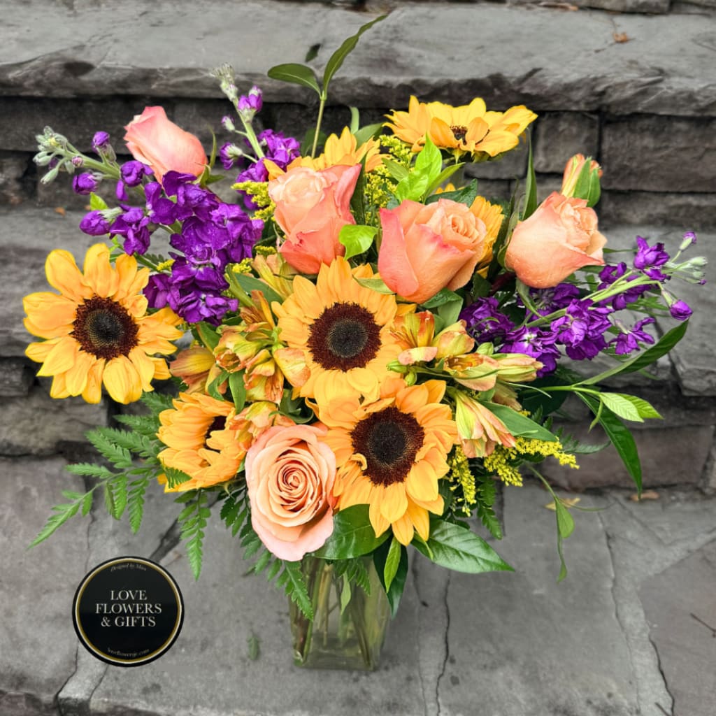 Bouquet of peach roses, sunflowers, and purple flowers in a glass vase