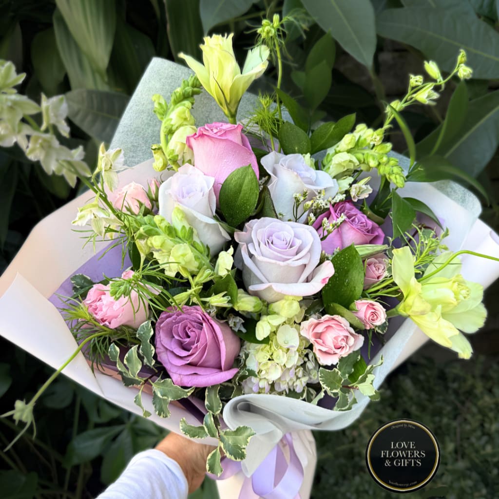 Handheld bouquet of pastel roses and pale yellow flowers wrapped in white paper