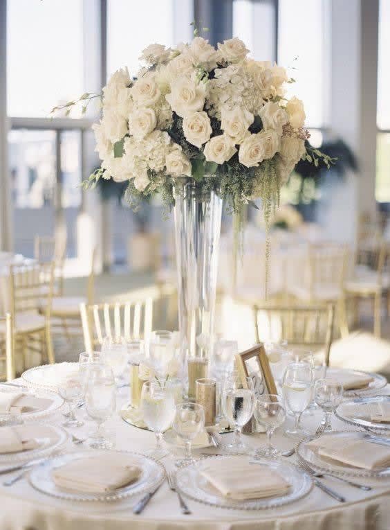 White rose centerpiece in a tall glass vase on a set dining table